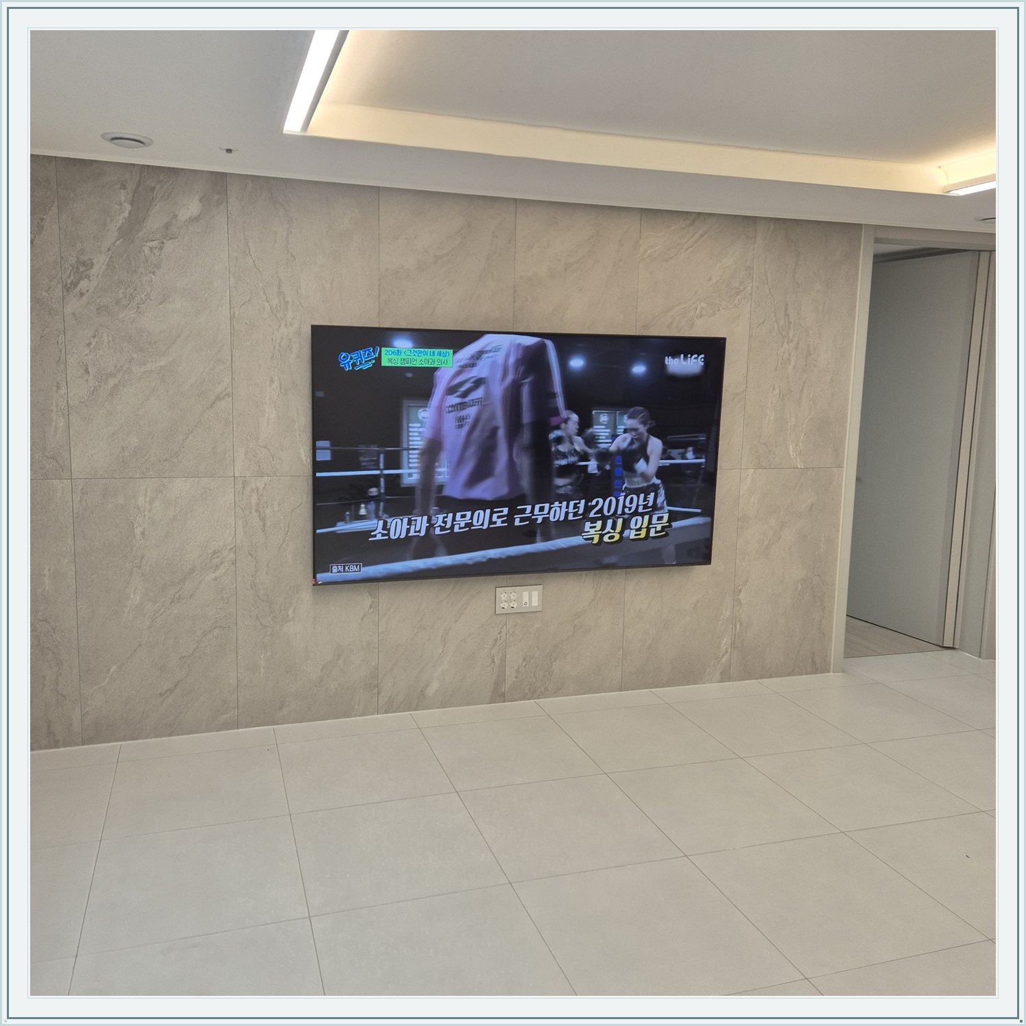 석재 느낌 벽면을 정면에서 본 TV, 넓은 바닥 여유와 조명 라인이 동시에 보입니다