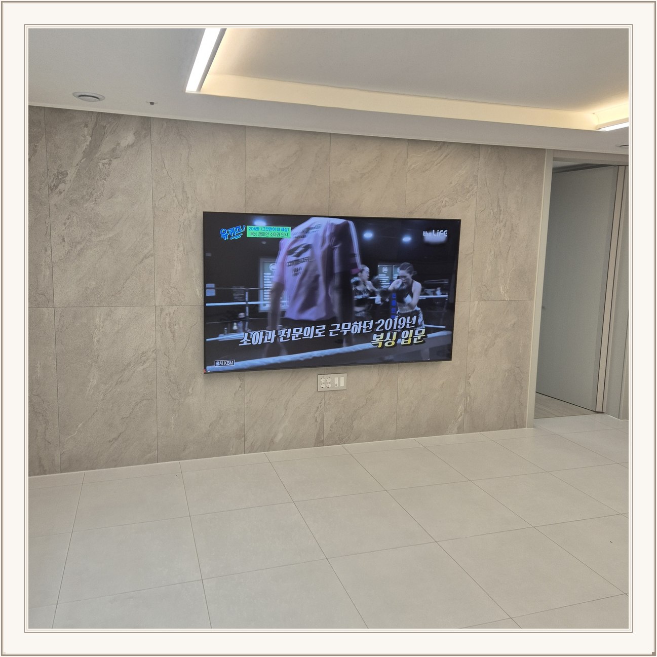 석재 느낌 벽면을 정면에서 본 TV, 벽 마감의 세로 이음선이 TV 양옆에 남아 있습니다