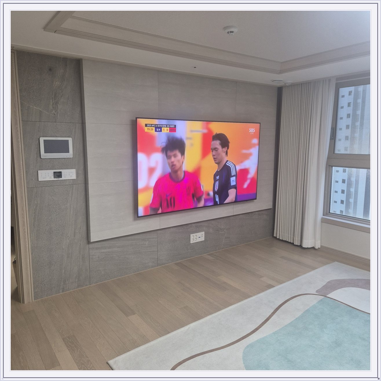 밝은 회색 아트월과 시청 공간, 밝은 몰딩과 TV 아래 전원 위치가 같이 나타납니다