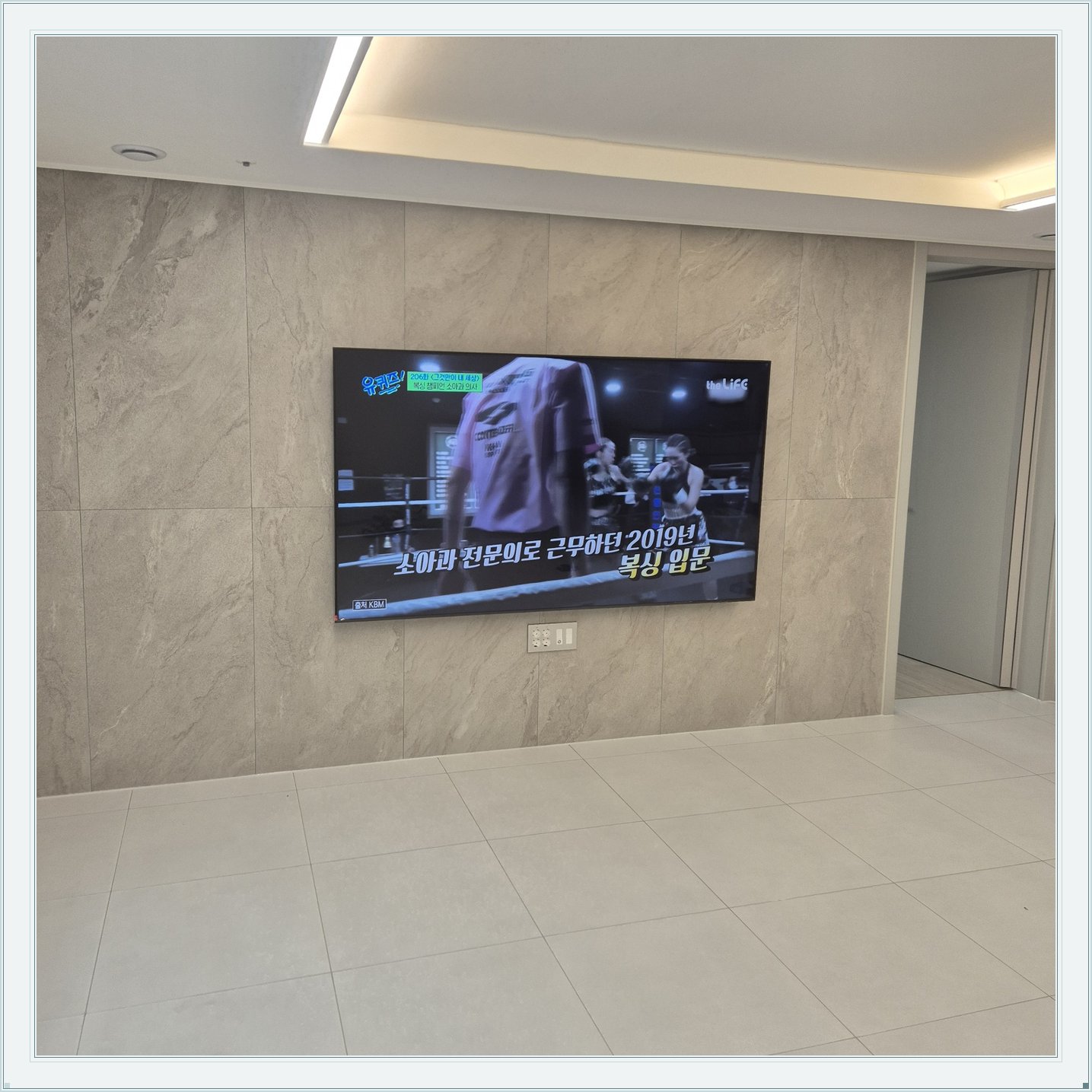 석재 느낌 벽면을 정면에서 본 TV, 벽 마감의 세로 이음선이 TV 양옆에 남아 있습니다