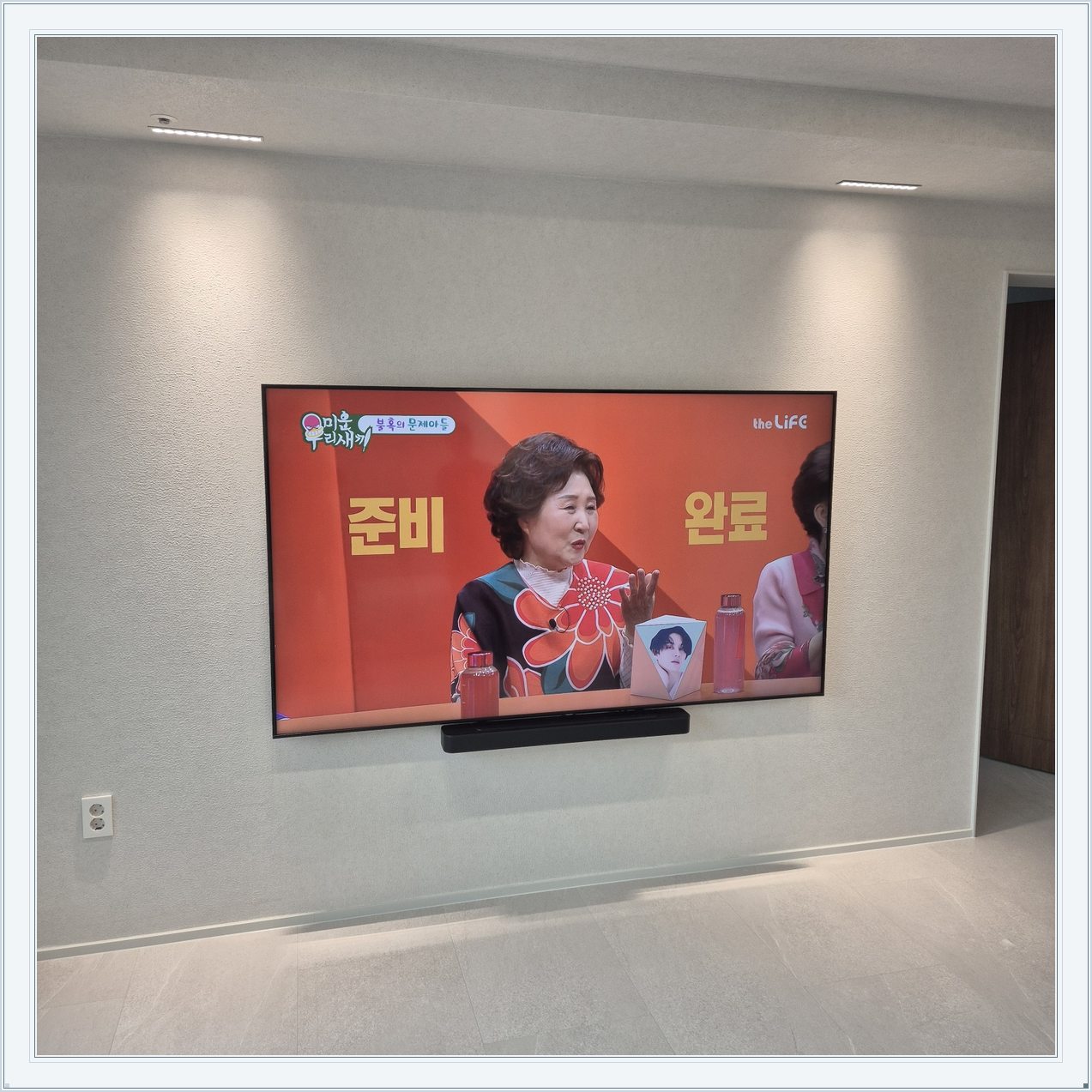 조명이 비추는 미색 벽과 사운드바, 사운드바와 벽면의 간격이 한눈에 들어옵니다