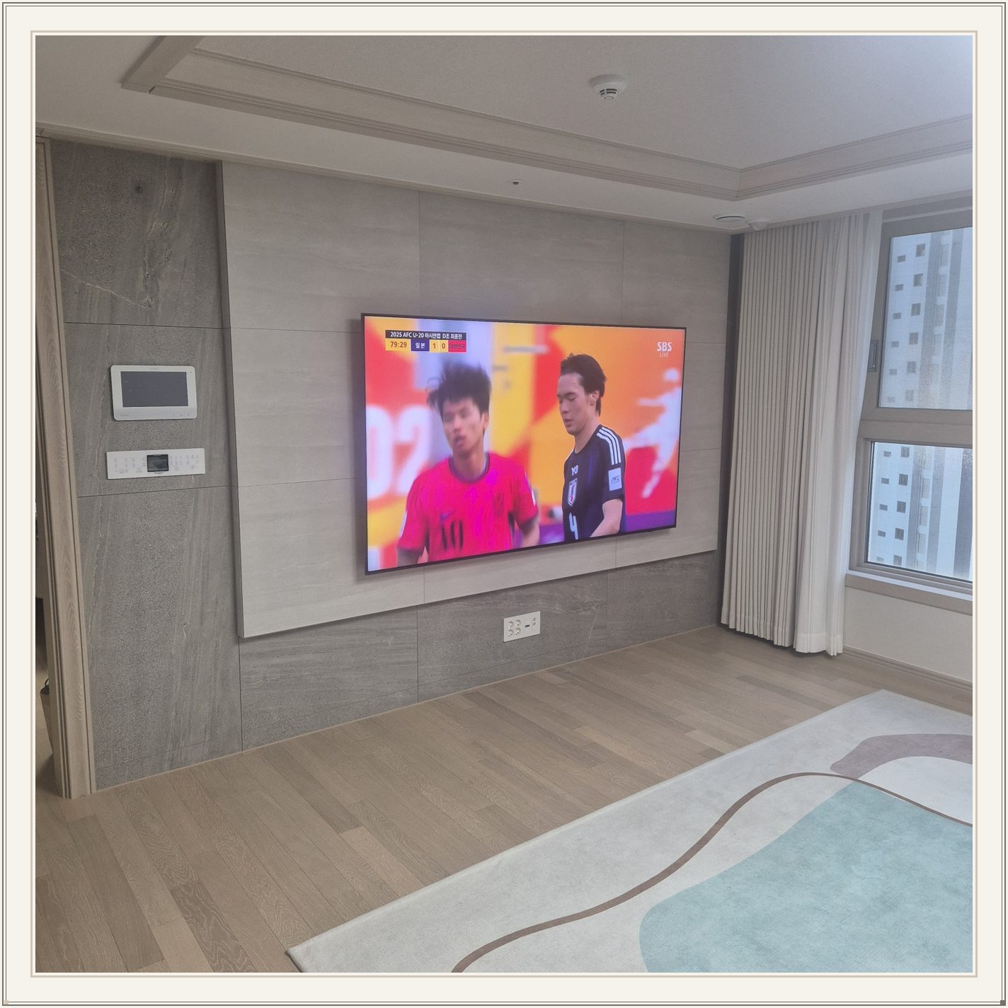 밝은 회색 아트월과 시청 공간, 밝은 몰딩과 TV 아래 전원 위치가 같이 나타납니다