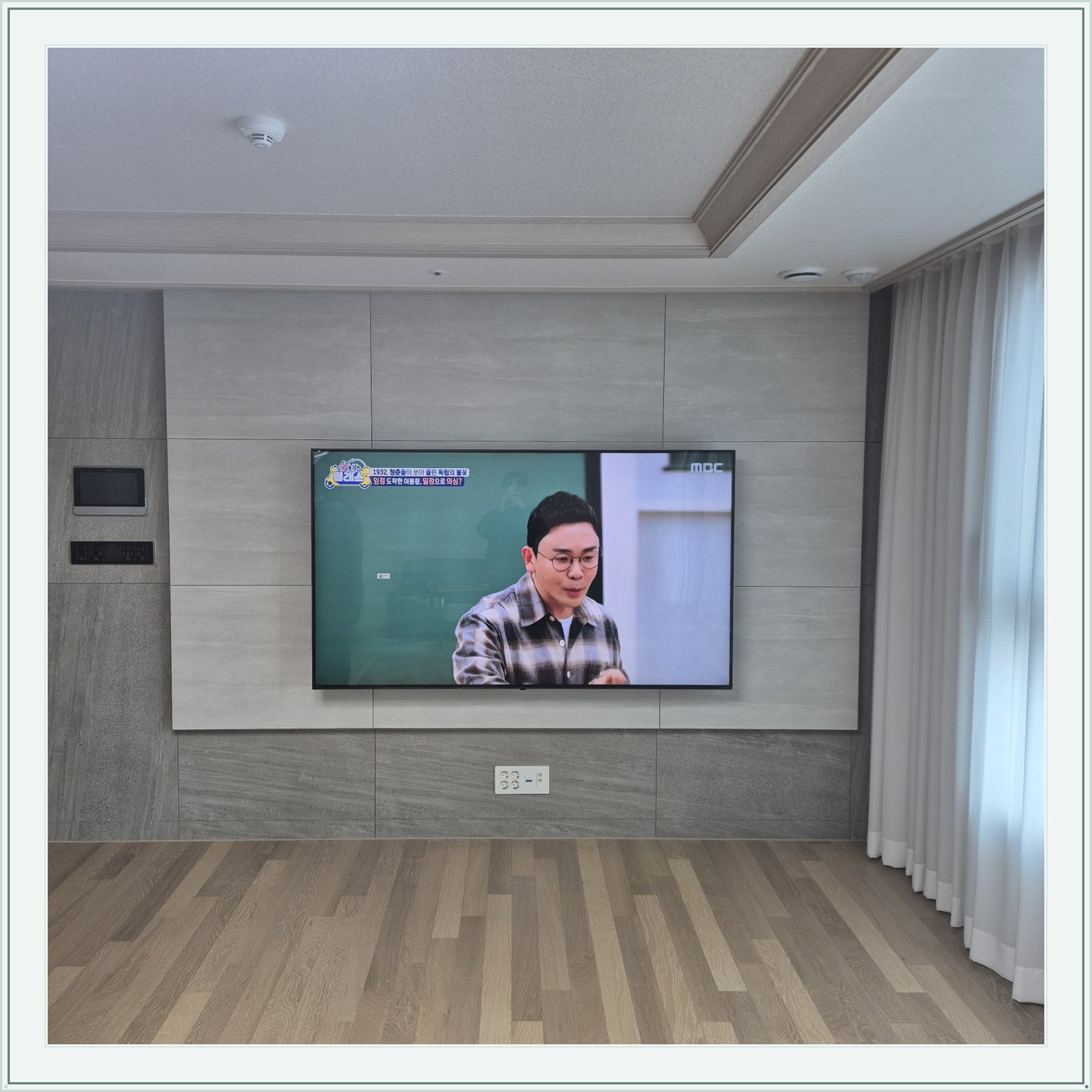 거실 회색 패널과 벽걸이 TV, TV 아래 콘센트와 양쪽 마감 판넬의 대비가 뚜렷합니다