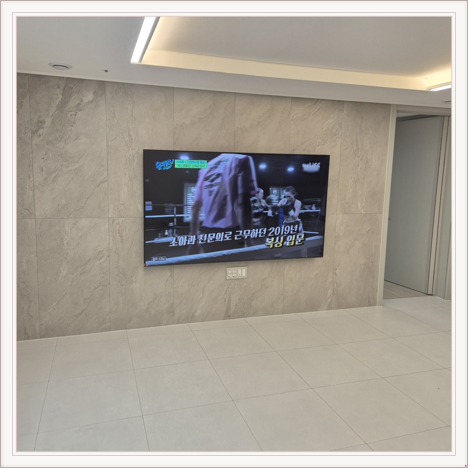 석재 느낌 벽면을 정면에서 본 TV, 벽 마감의 세로 이음선이 TV 양옆에 남아 있습니다